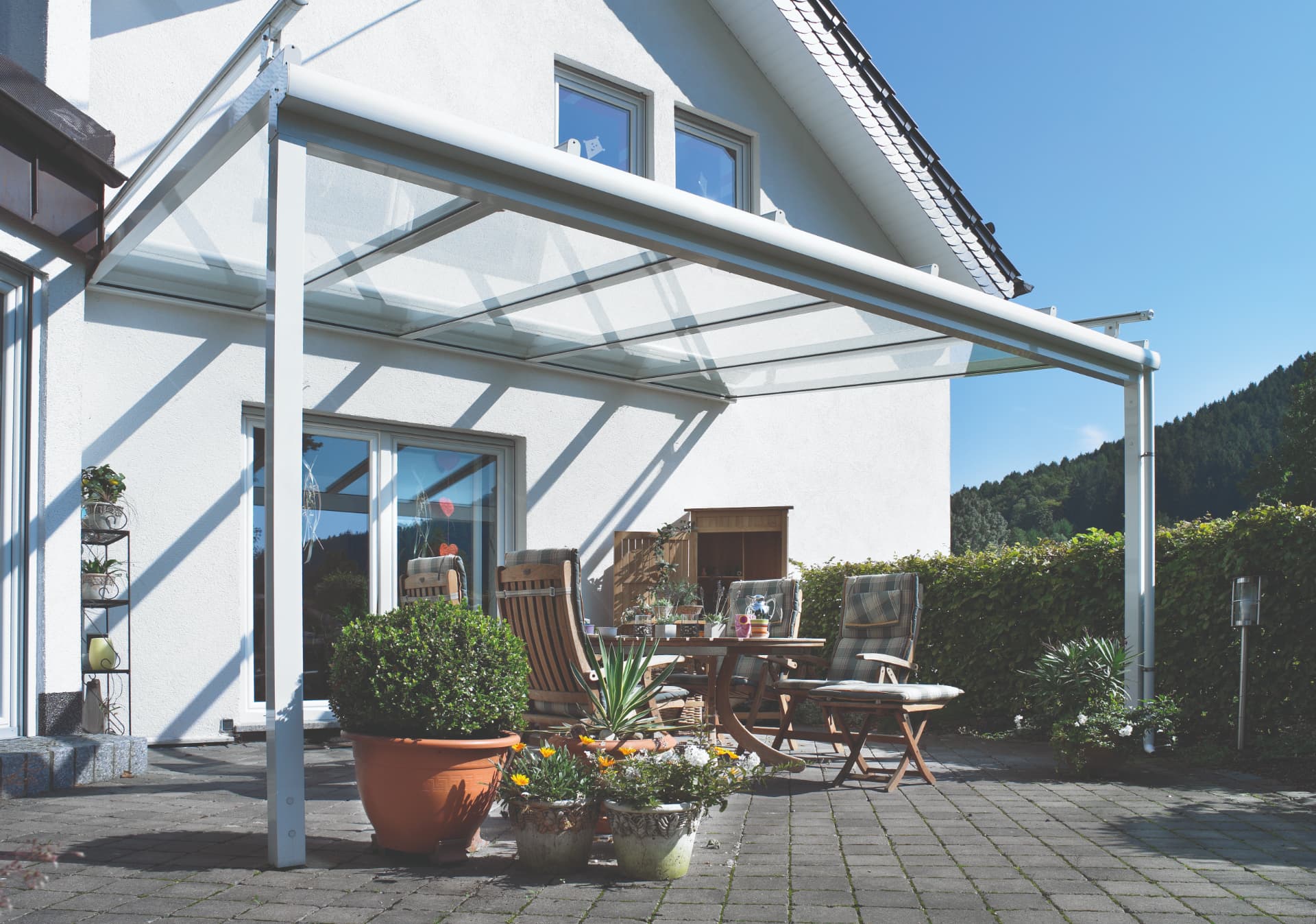 Glasvordach mit weißer Metallkonstruktion und Markise über einer Terrasse mit Pflanzenschutz