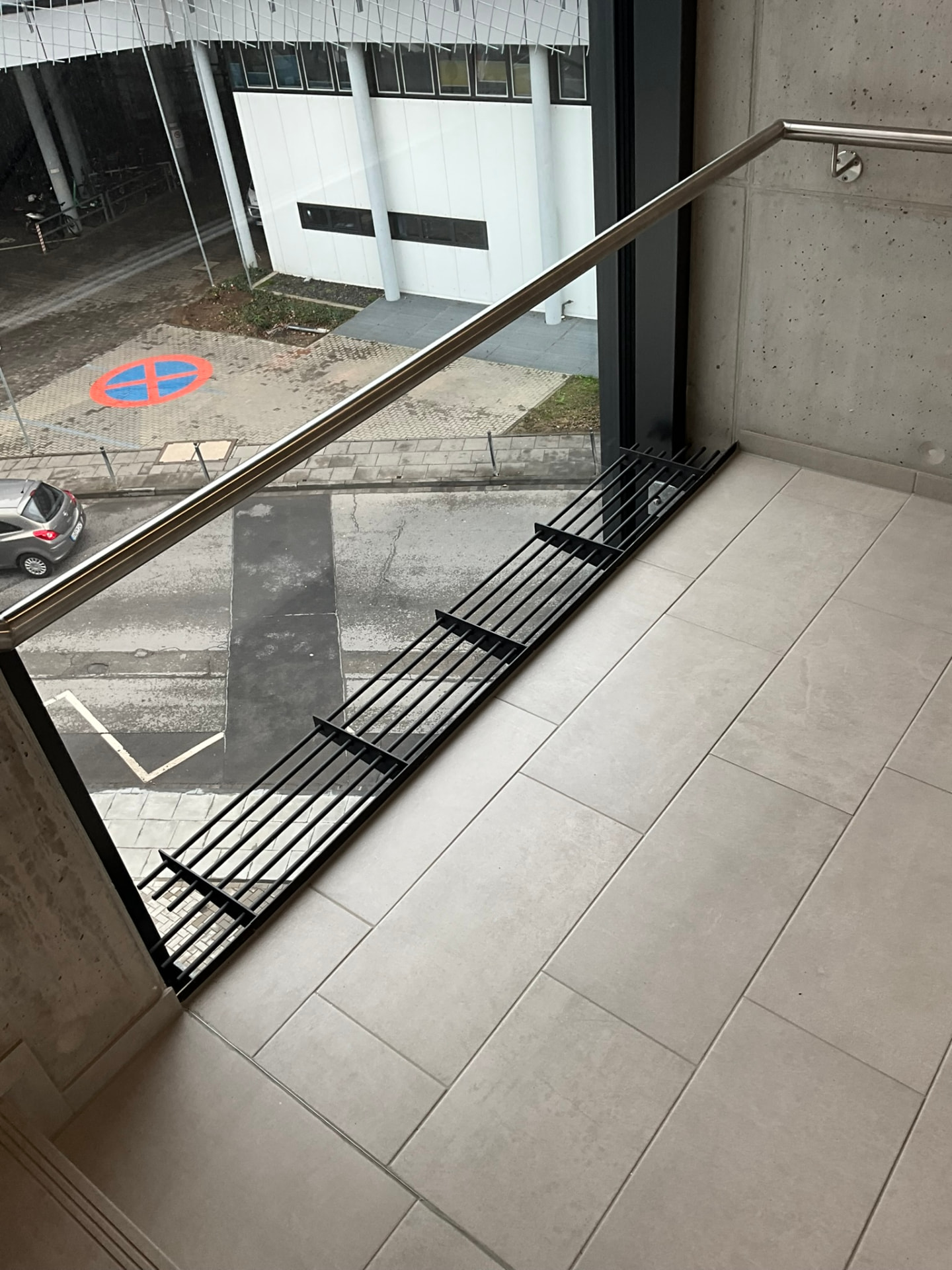 Absturzsicherung mit Edelstahl-Rundhandlauf und bodenbündigem Lüftungsgitter an einem Balkon