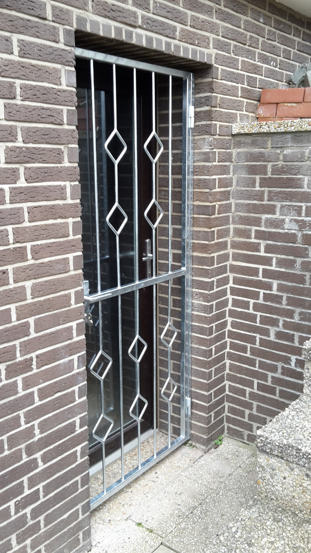 Schwenkbare Sicherheitstür aus verzinktem Stahl mit Rautenmuster vor einer Eingangstür