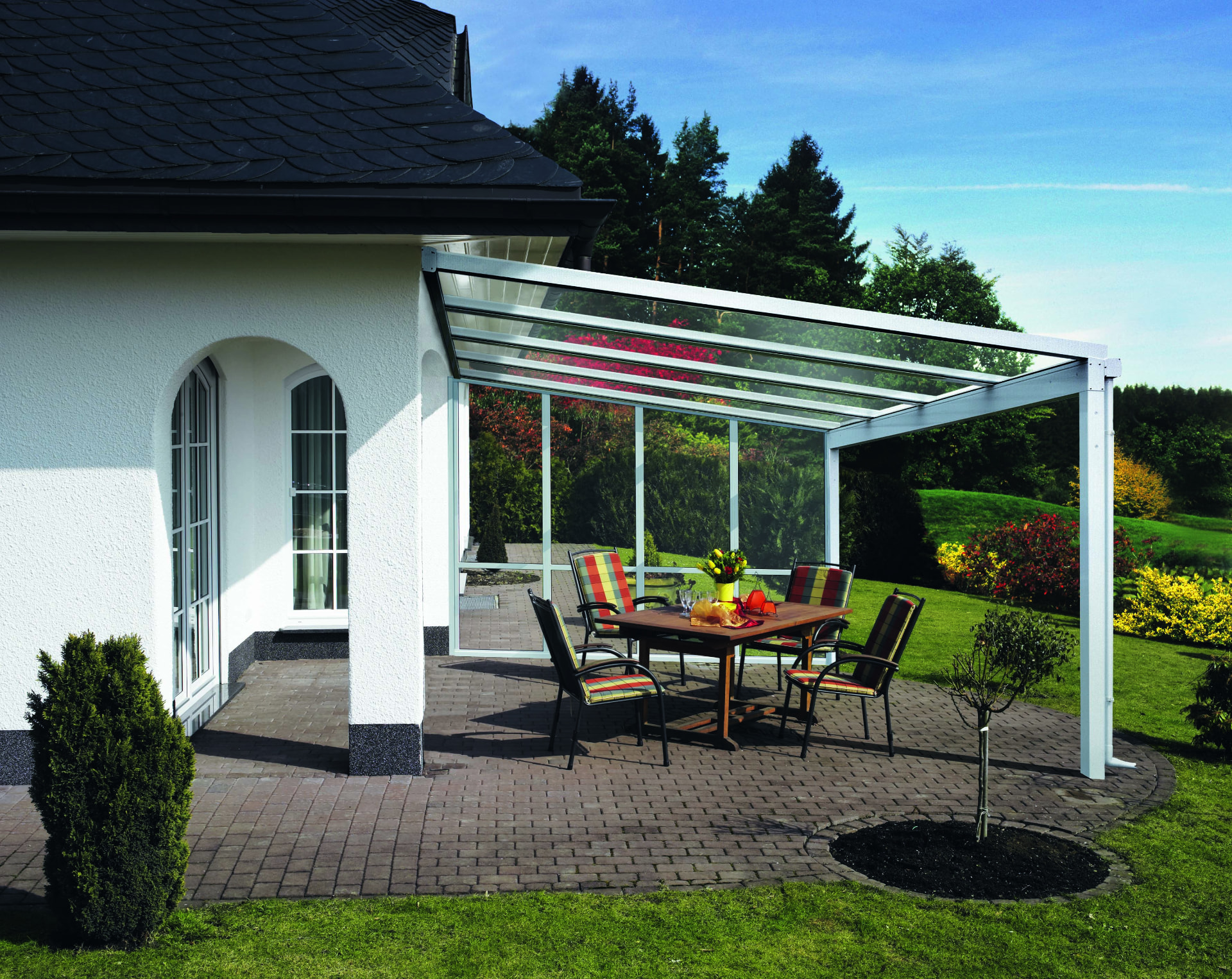 Terrassenüberdachung aus Glas mit weißer Stahlkonstruktion über einem Sitzbereich auf einer Gartenterrasse