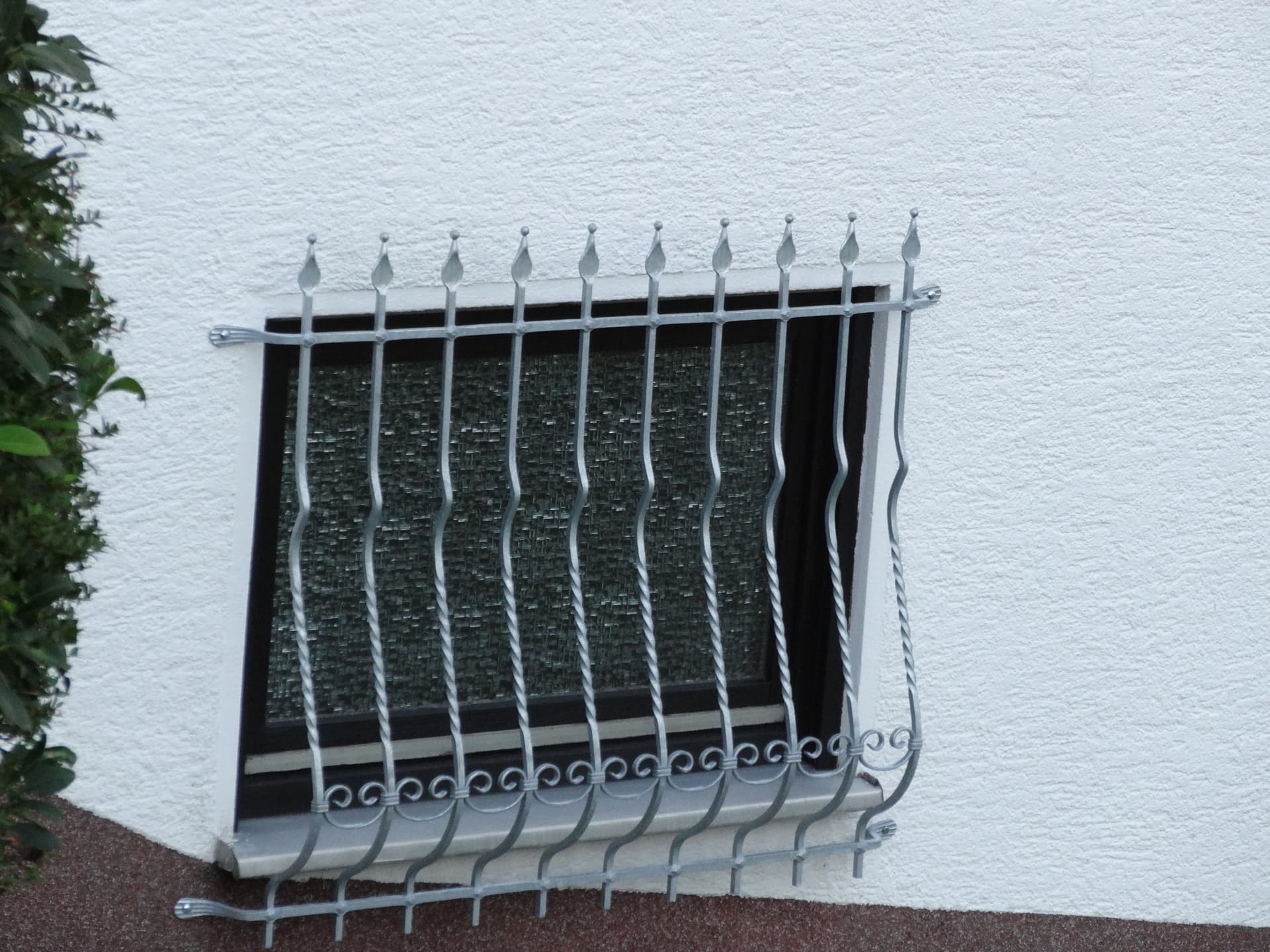Fenstergitter mit Zierspitzen und geschweiften Stäben vor einem Kellerfenster